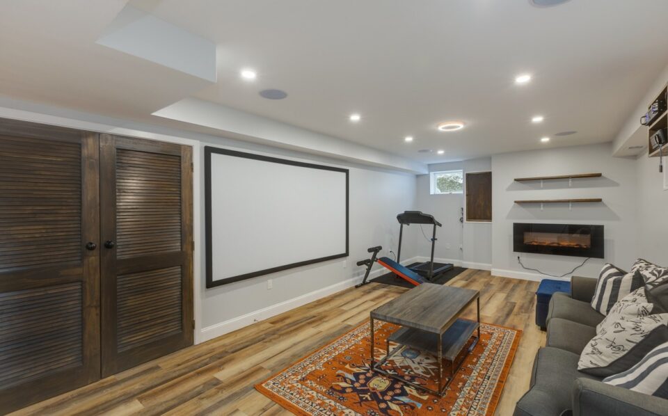 Basement after remodel - recessed lighting, vinyl plank flooring, projector wall and electric fireplace