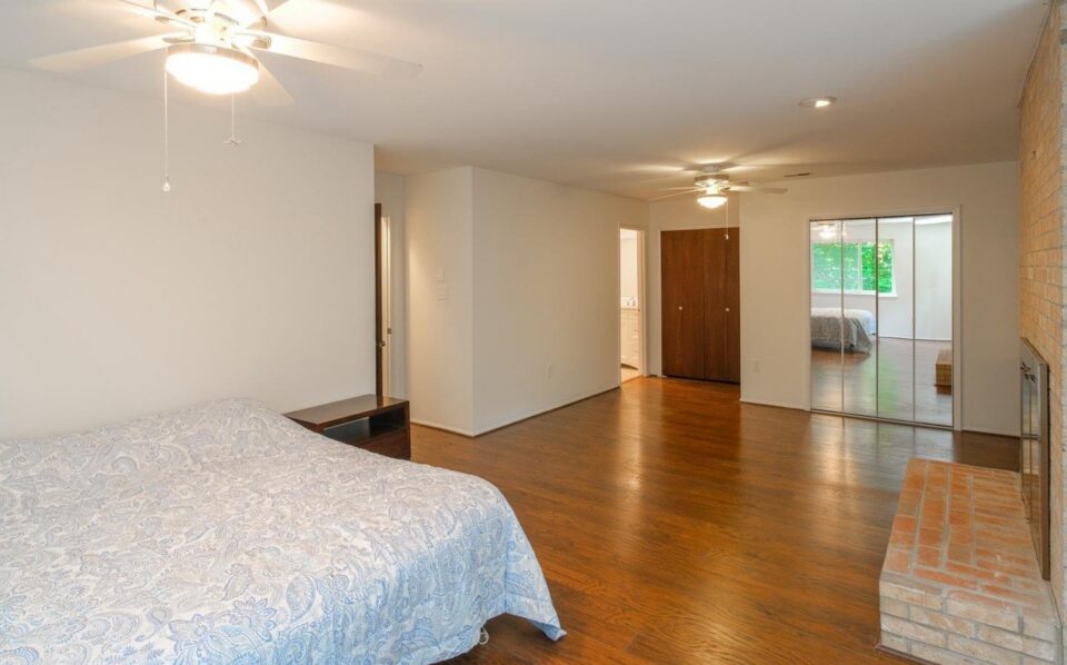 Bedroom before remodel - ceiling fans, mirrored closet doors and a brick fireplace