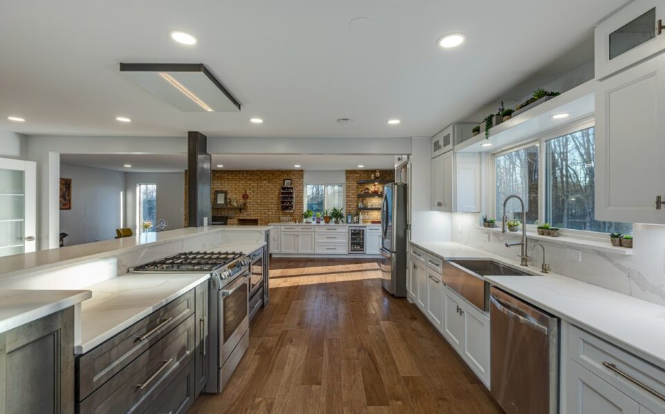Kitchen after remodel - long quartz island with a gas range, white shaker cabinets and wide-plank flooring