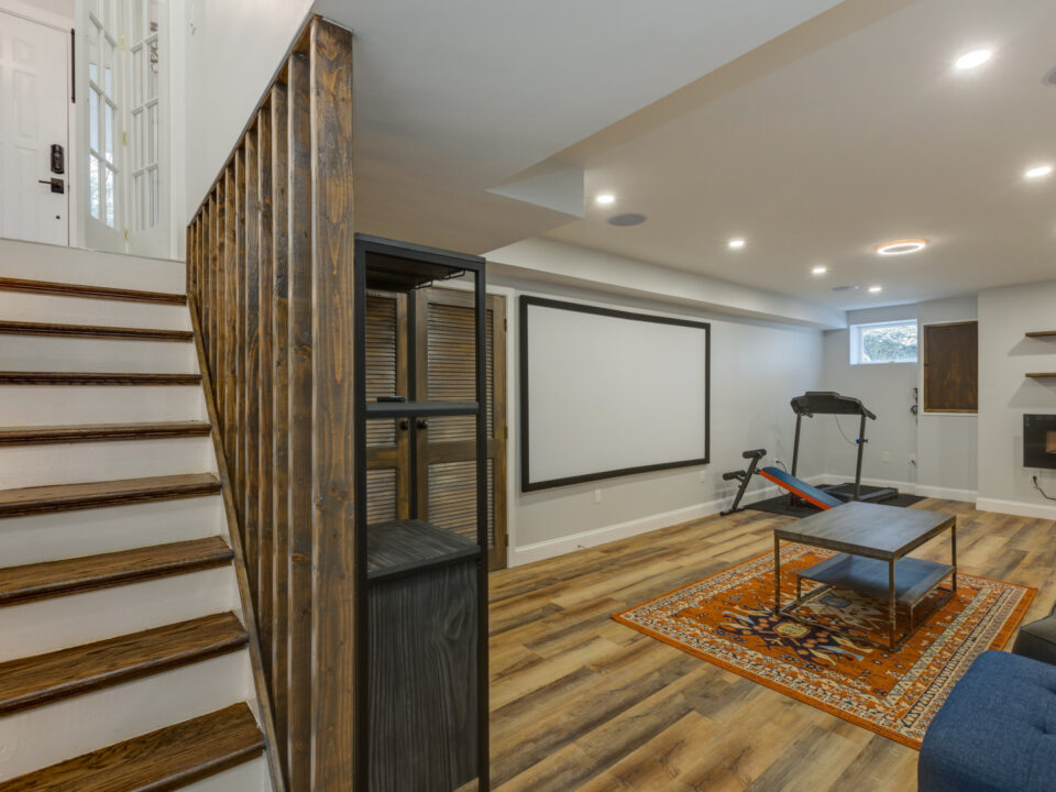 Finished basement rec room with wood stairs, projector screen and home gym area